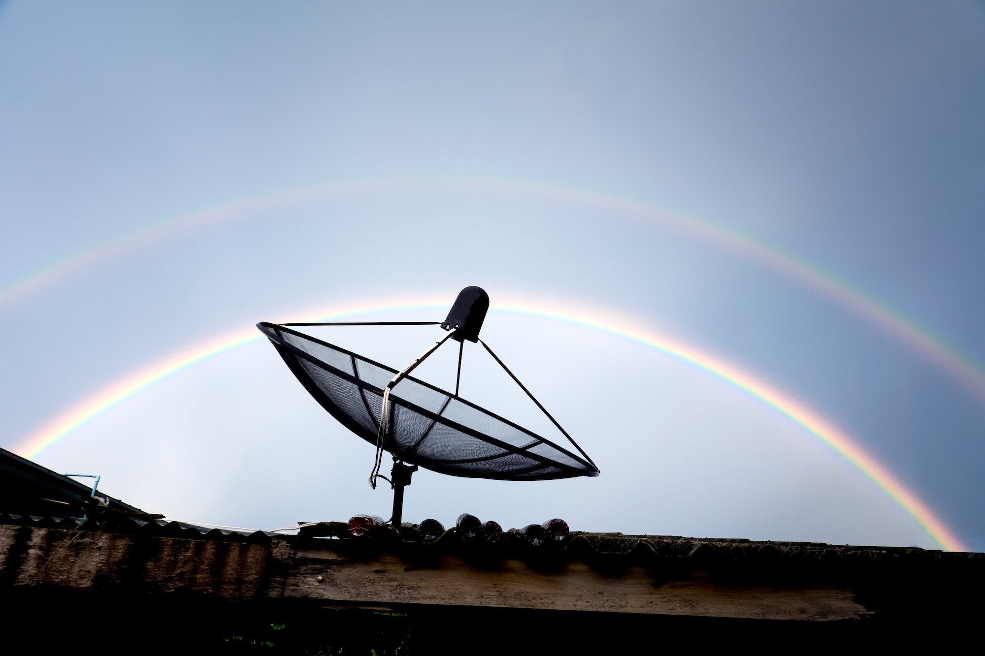satellite dish on the roof against rainbow sky